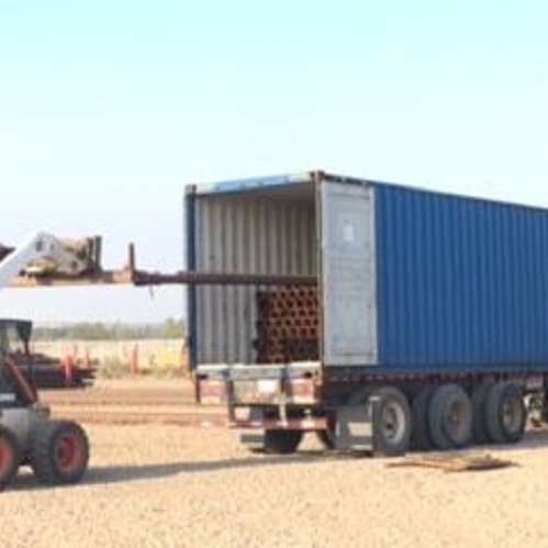 Image of a truck loader loading metal pipes into a trailer truck